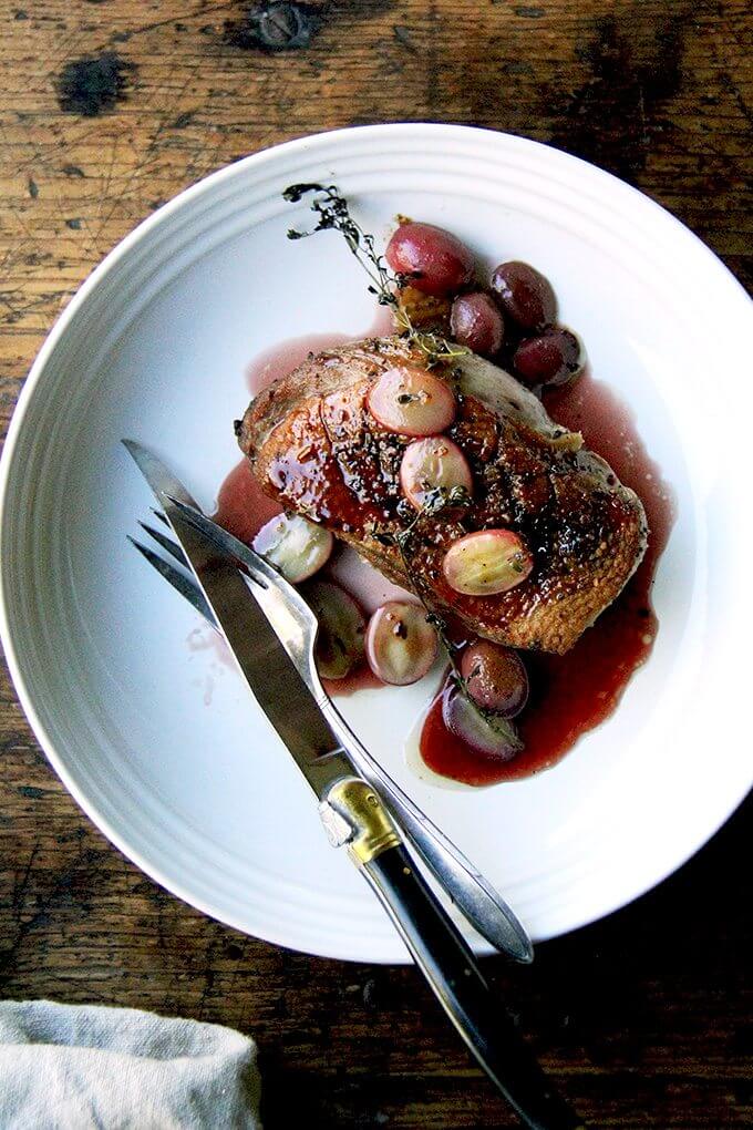 A plate of duck breast, gastrique, roasted grapes and thyme. 