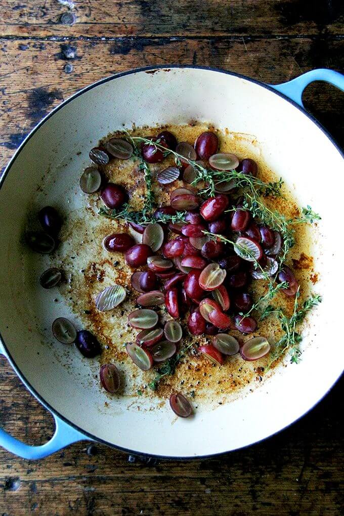 A Le Creuset braiser filled with grapes and thyme.