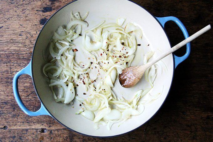 An overhead shot of an onion being sautéed with crushed red pepper flakes.