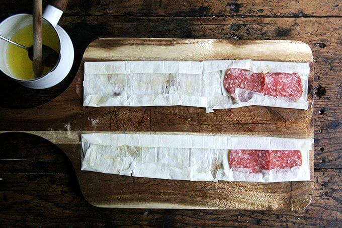 Phyllo on a cutting board, brushed with butter, topped with provolone and salami, edges folded in.