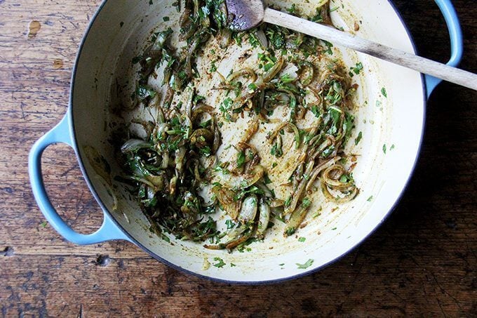 A Le Creuset braiser filled with sautéed onions and cilantro.