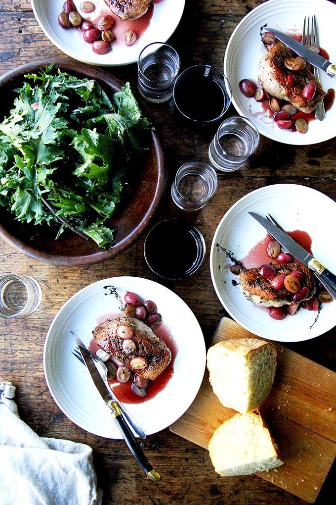 Overhead shot of a table set with 4 plates of duck breast, salad, bread, wine, and water.