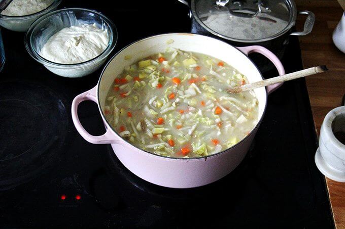 An overhead shot of a stovetop holding a large pot of cabbage soup and two bowls of rising bread dough. 