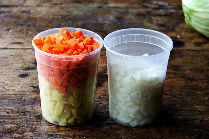 Two quart containers filled with chopped vegetables: carrots, potatoes, and onions.