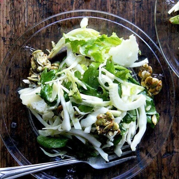 Two plates of a fall salad with cabbage, fennel, greens, and candied pepitas.