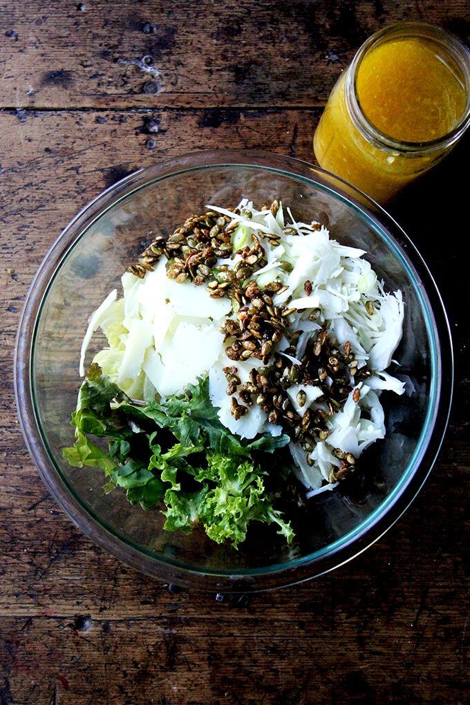 A large bowl with ingredients for a fall salad with dressing in a jar on the side.