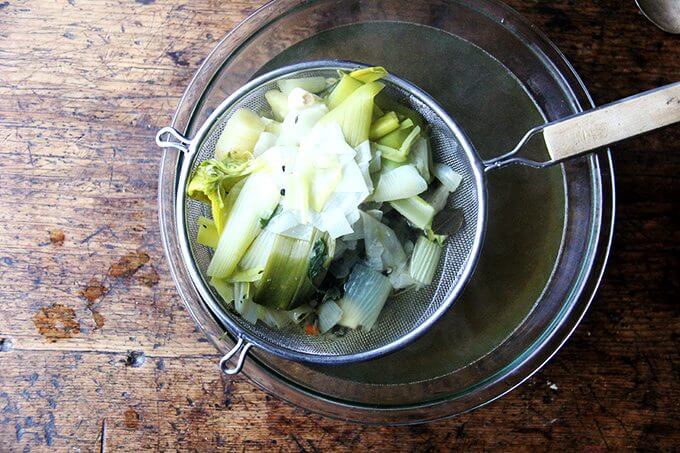 A strainer holding cooked vegetables over a bowl of vegetable stock. 