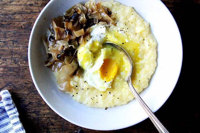 A bowl of polenta topped with a poached egg, broken into. 