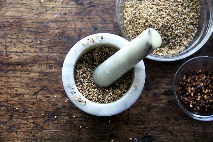 A mortar and pestle with cumin, coriander, and sesame seeds.