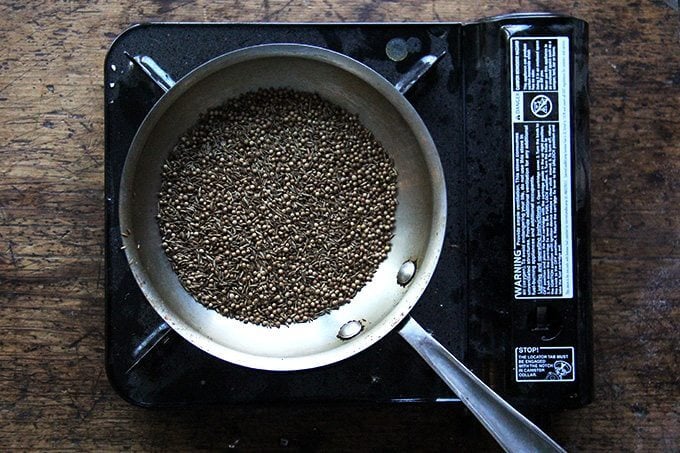 A skillet with cumin and coriander seeds on a portable burner.