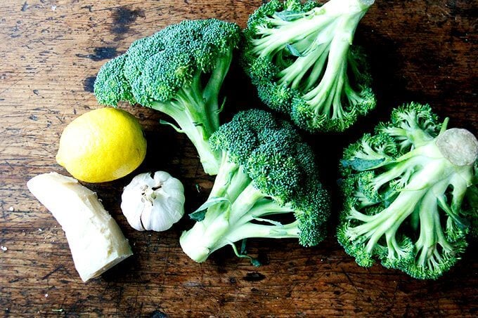 Three heads of broccoli, a lemon, a head of garlic, and a block of parmesan.