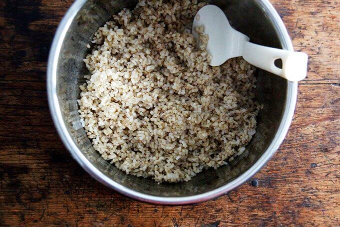 An uncovered Instant pot filled with perfectly cooked Instant Pot brown rice and a plastic spoon. 