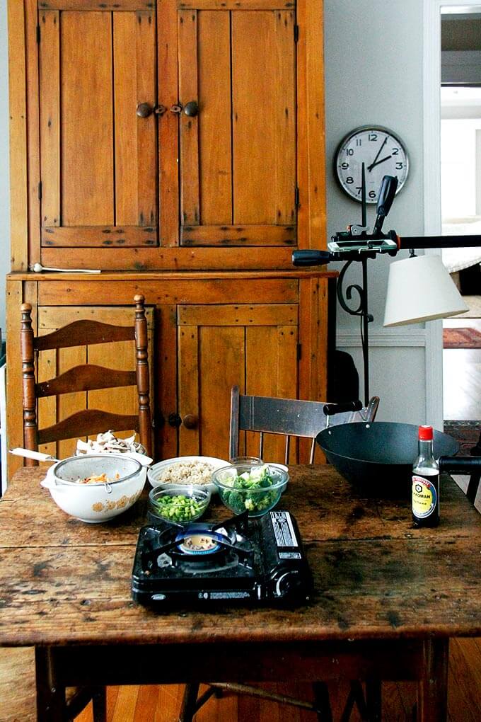 A makeshift kitchen: gas burner on table aside wok.