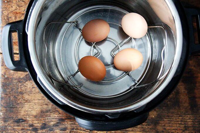 Overhead shot of instant pot with steamer basket inserted, 4 eggs on top, and 2 cups of water.