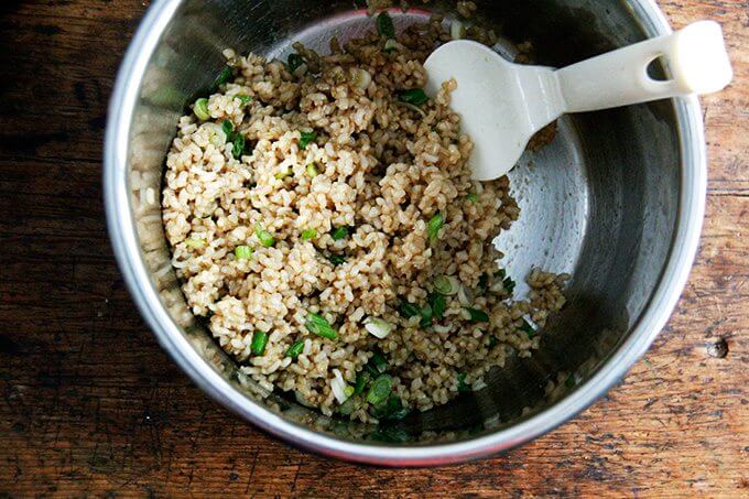 An uncovered Instant pot filled with perfectly cooked Instant Pot brown rice, scallions, and seasonings all tossed together.