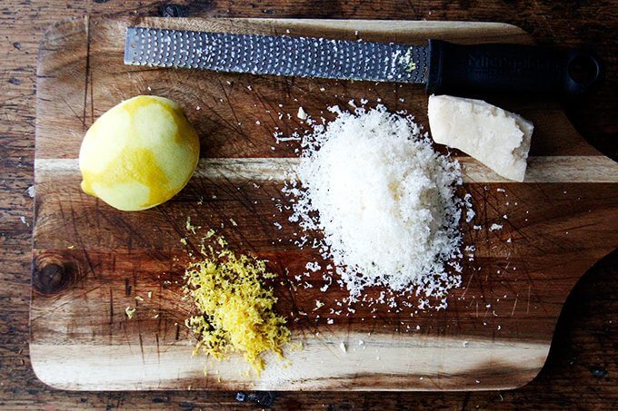 A board with lemon zest and grated parmesan and a microplane grater.