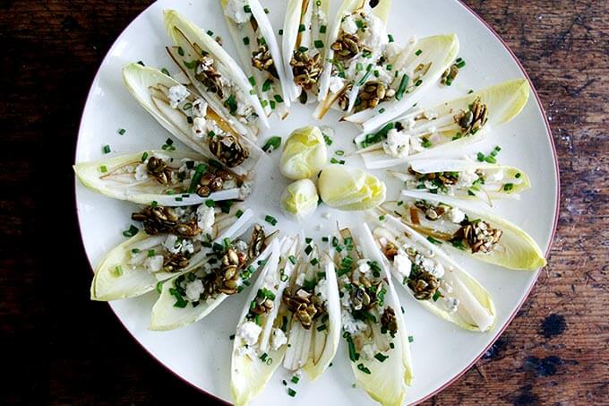 A platter of endive boats with slivered pears and blue cheese and candied pepitas and chopped chives.