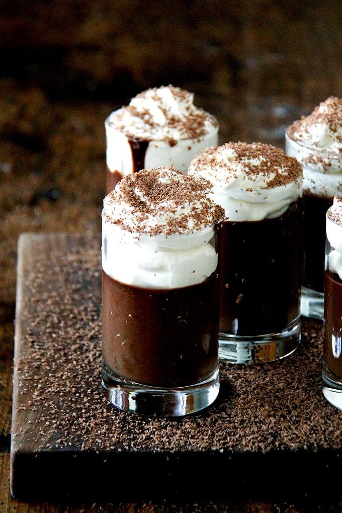 A board filled with small glasses filled with chocolate pot de creme and topped with homemade whipped cream.