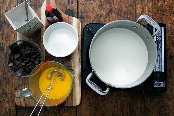 Overhead shot of a pot of cream on a portable burner aside other ingredients for stovetop pot de creme. 