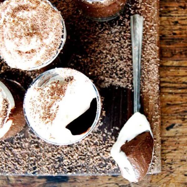 A board filled with small glasses filled with chocolate pot de creme and topped with homemade whipped cream.