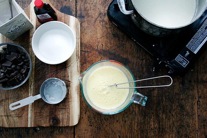 A liquid measure filled with yolks and hot cream being tempered with a whisk.