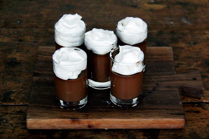 A board filled with small glasses filled with chocolate pot de creme and topped with homemade whipped cream.