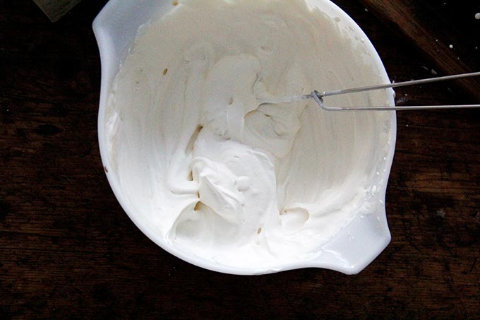 A large bowl filled with homemade whipped cream and a wire whip.