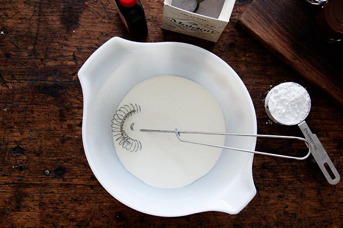 A large bowl filled with heavy cream and a wire whip.