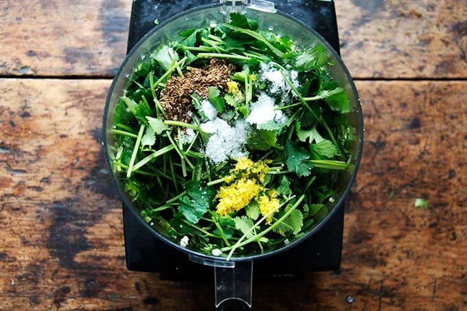 A food processor filled with herbs, spices, salt, lemon zest, garlic, and chilies.