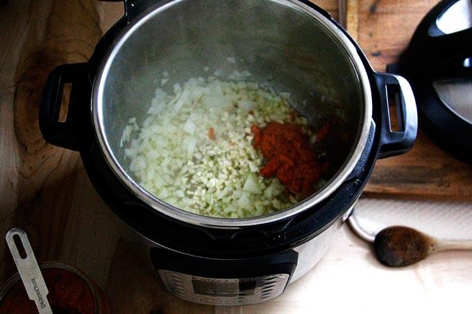 An Instant Pot with onion, garlic, and harissa.