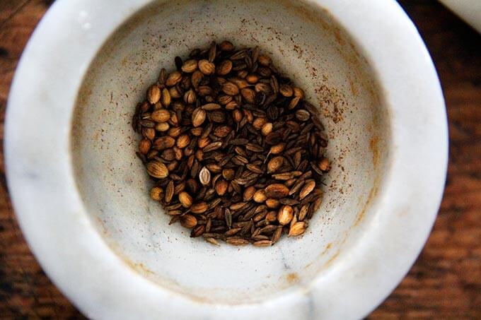 A mortar and pestle filled with toasted cumin and coriander.