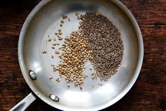 A skillet with cumin and coriander seeds in it.