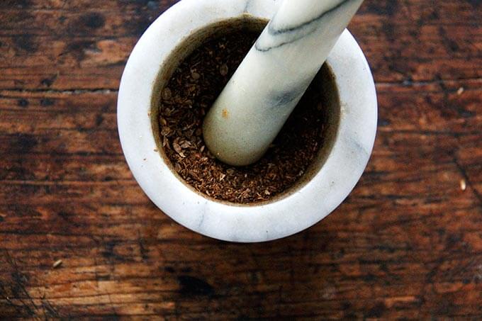 A mortar and pestle with ground cumin and coriander seeds in it.