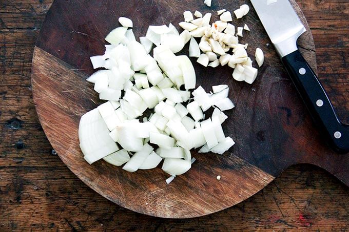 A cutting board with chopped onion and garlic.