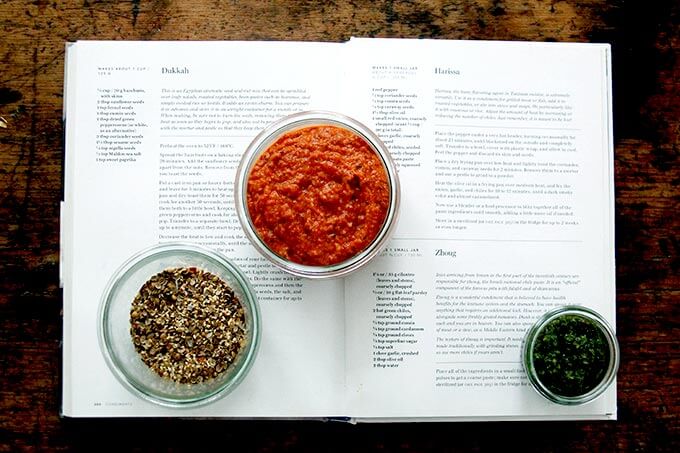 A cookbook open to the condiments page with recipes for harissa, dukkah, and skhug.