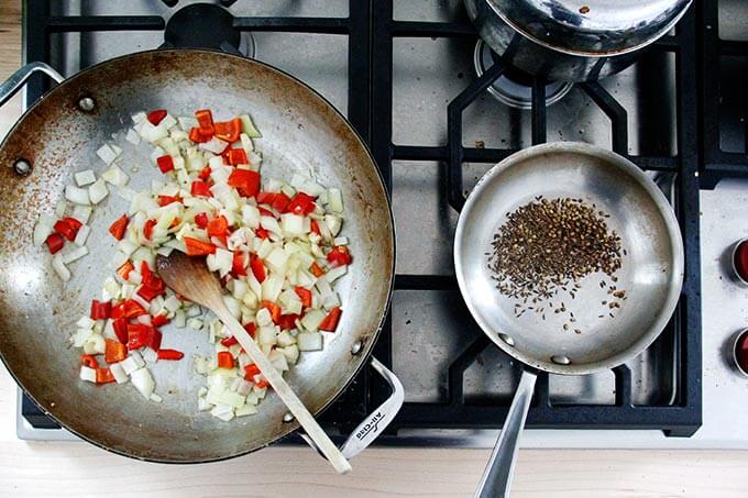 An overhead shot of a skillet with sautéed onions and chilies and a smaller skillet with cumin and coriander.