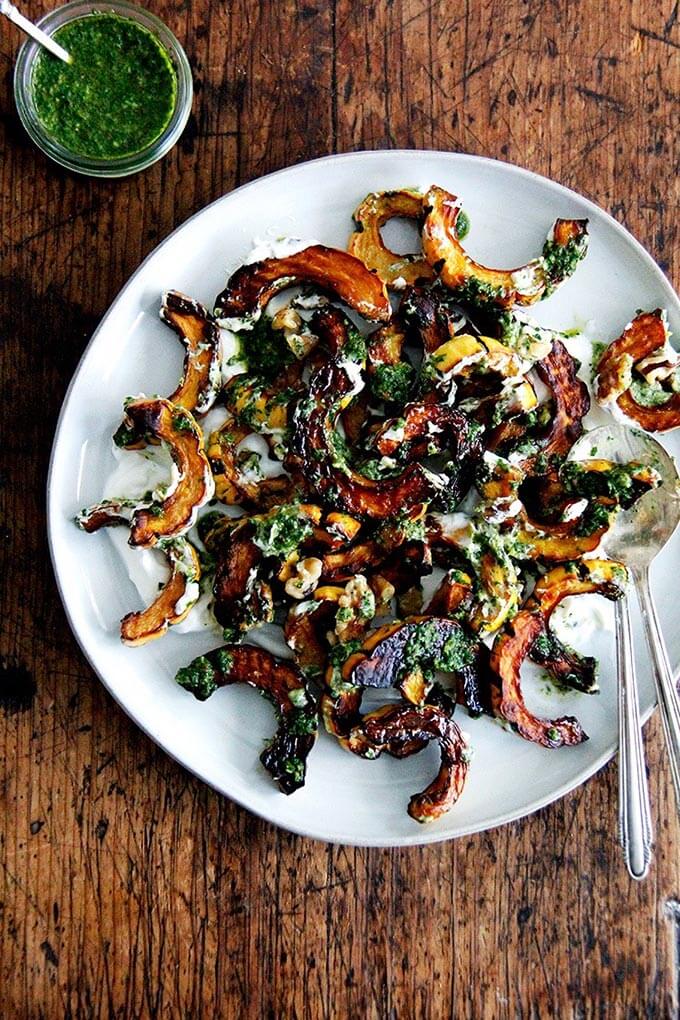 A plate of roasted delicata squash with schug and lemony yogurt sauce.