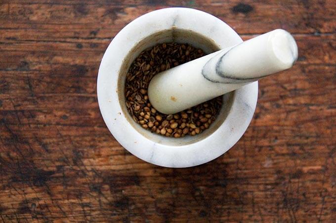 A mortar and pestle with cumin and coriander seeds in it.