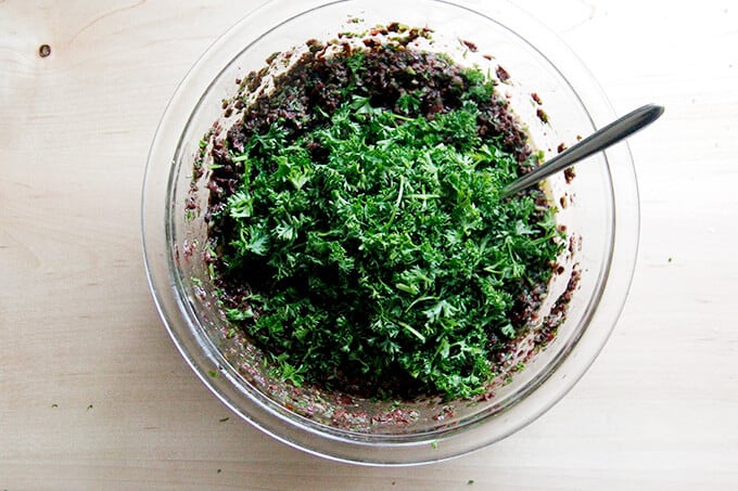 A bowl of black olive tapenade topped with a heap of freshly chopped parsley.
