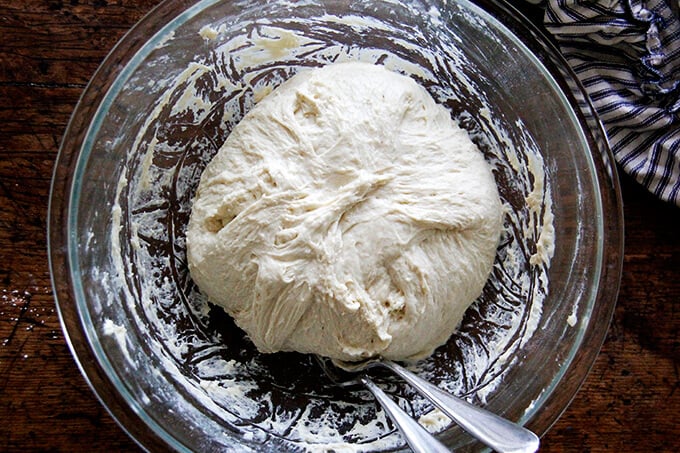 A glass bowl filled with brioche dough punched down. 