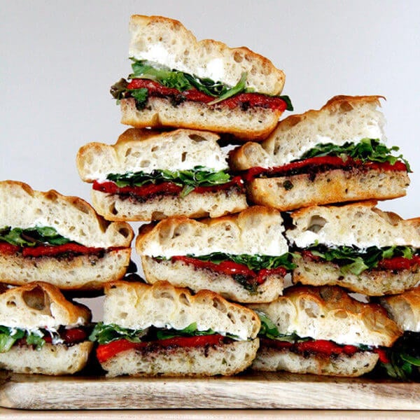 A stack of slab sandwiches with whipped honey goat cheese, roasted red peppers, olive tapenade and greens.