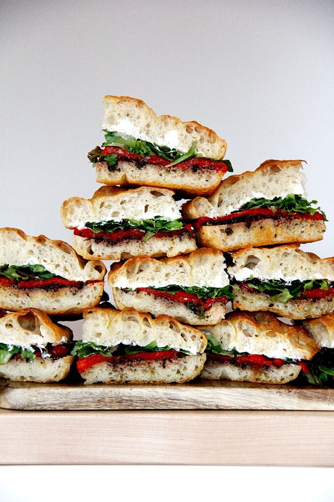 A stack of sandwiches with black olive tapenade, roasted red peppers, whipped honey goat cheese, and lettuce.