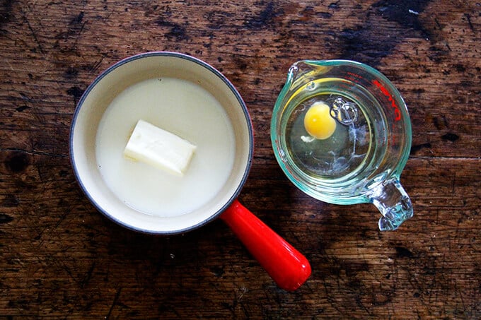 A pot with butter and milk aside a liquid measure with an egg and water.
