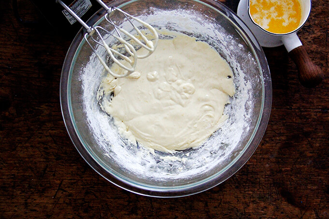 An overhead shot of a bowl of madeleine cookie batter aside a small sauce pan holding melted butter.