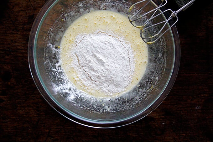 An overhead shot of a bowl of eggs beaten with sugar, lemon zest and flour.