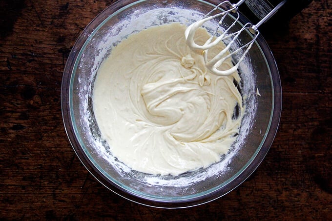 An overhead shot of a madeleine batter in a large bowl aside a hand-held mixer.