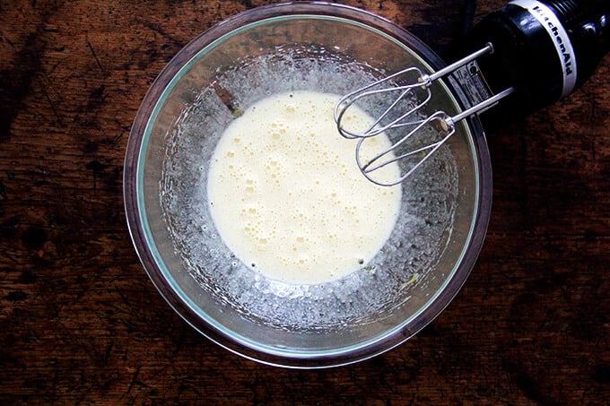 An overhead shot of a bowl of eggs beaten with sugar aside a hand-held mixer.