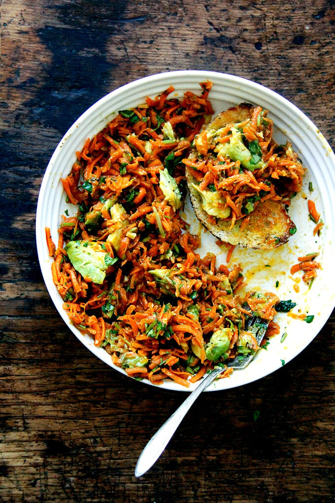 A bowl of Moroccan carrot salad with bread and avocado.