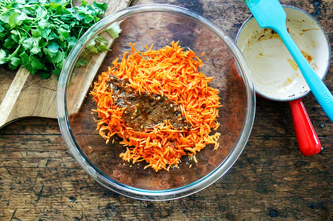 A large bowl filled with grated carrots and warm harissa dressing. 