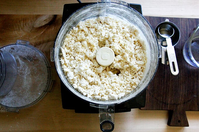 A counter with a food processor filled with dry ingredients pulsed with butter and ice water.